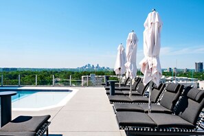 A rooftop pool area with lounge chairs and umbrellas, a clear view of a city skyline in the background. - The Tess, Autograph Collection (Atlanta)