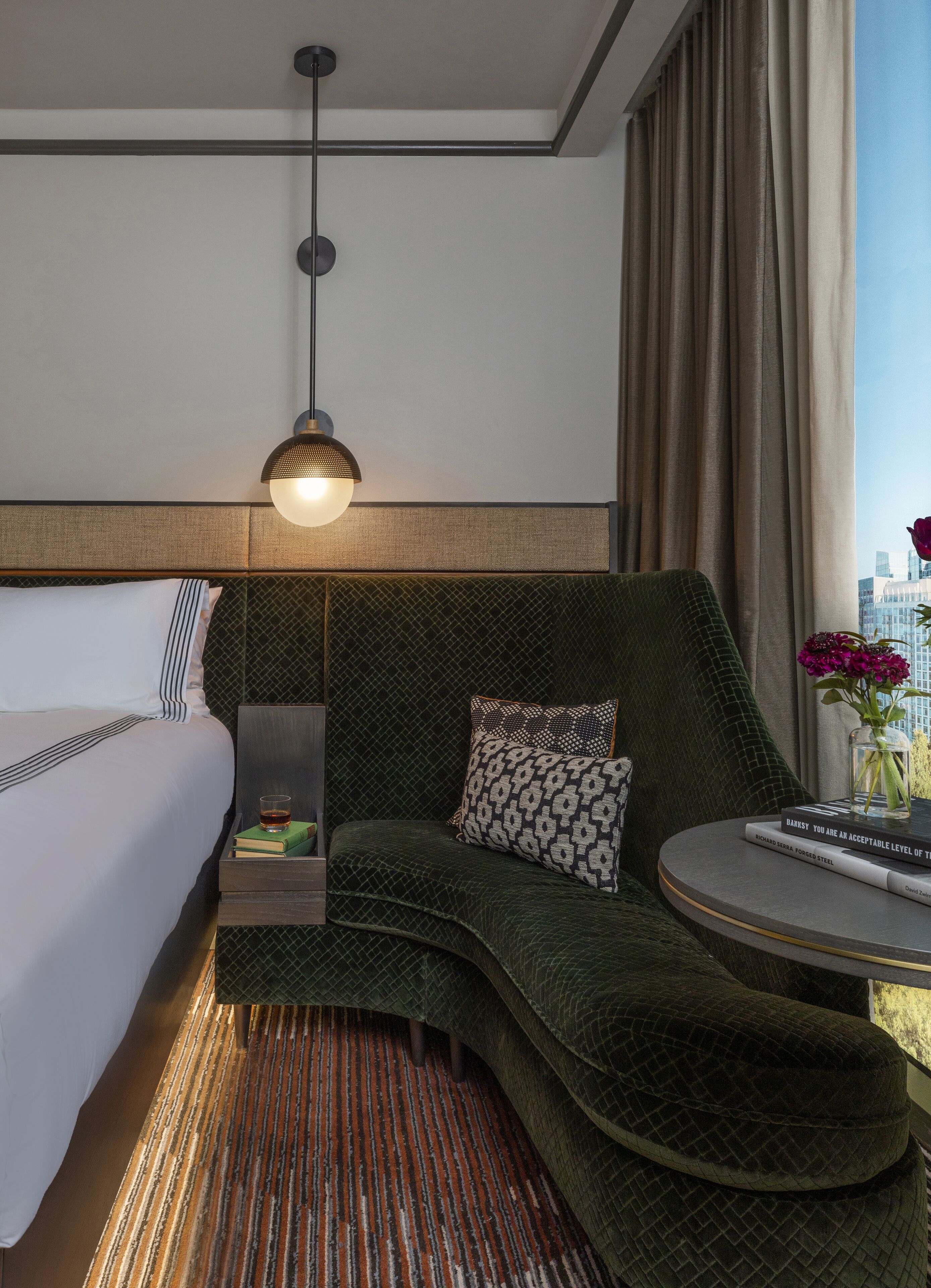 Ein Hotelzimmer mit Bett, einer Couch, einem kleinen Tisch, einer Vase mit Blumen und Blick auf die Stadt.