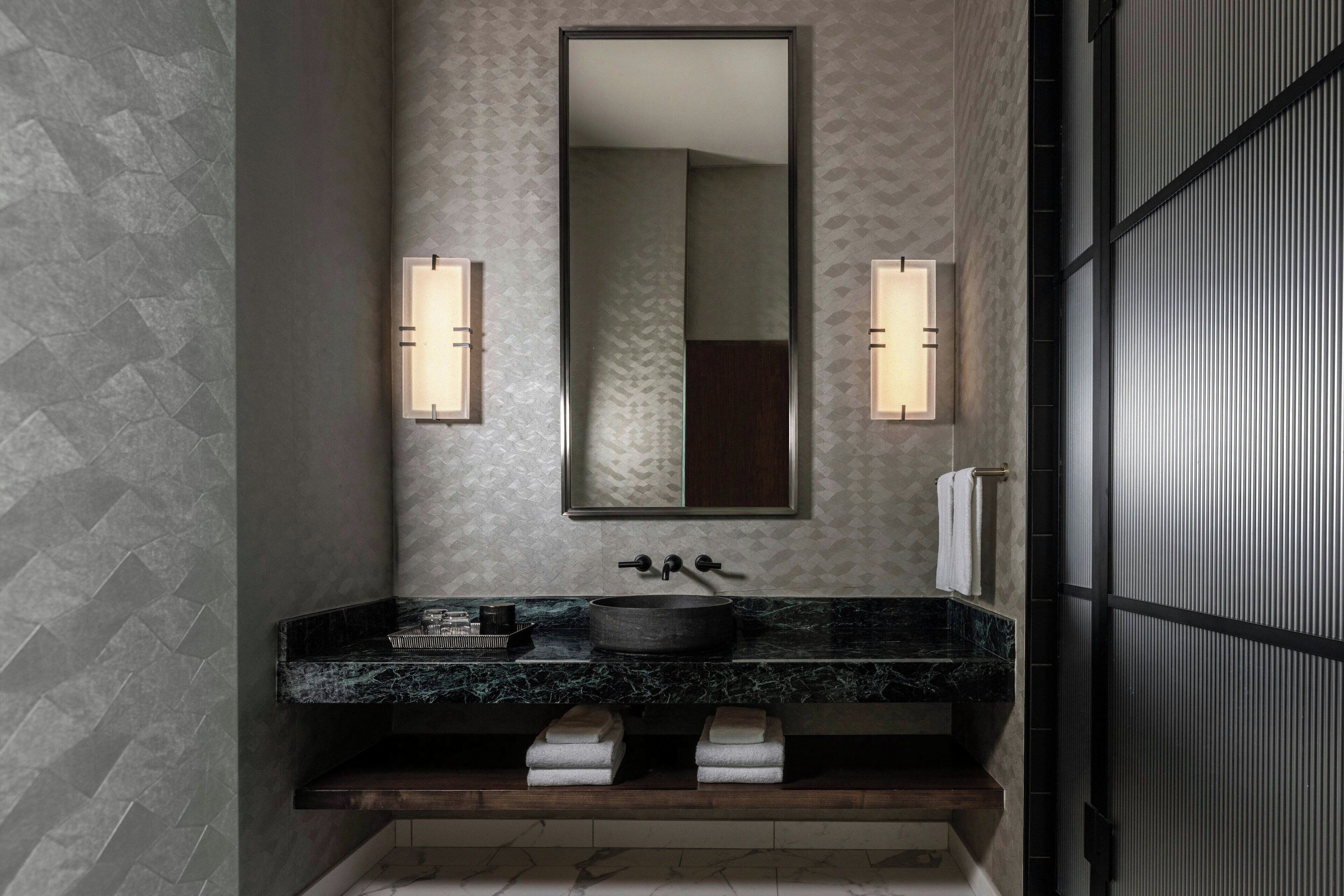 Un baño con lavamanos de mármol negro, un espejo grande y dos luces empotradas.