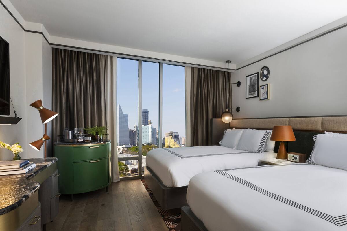 A hotel room with two beds, a green minibar, a city view, and a modern decor.