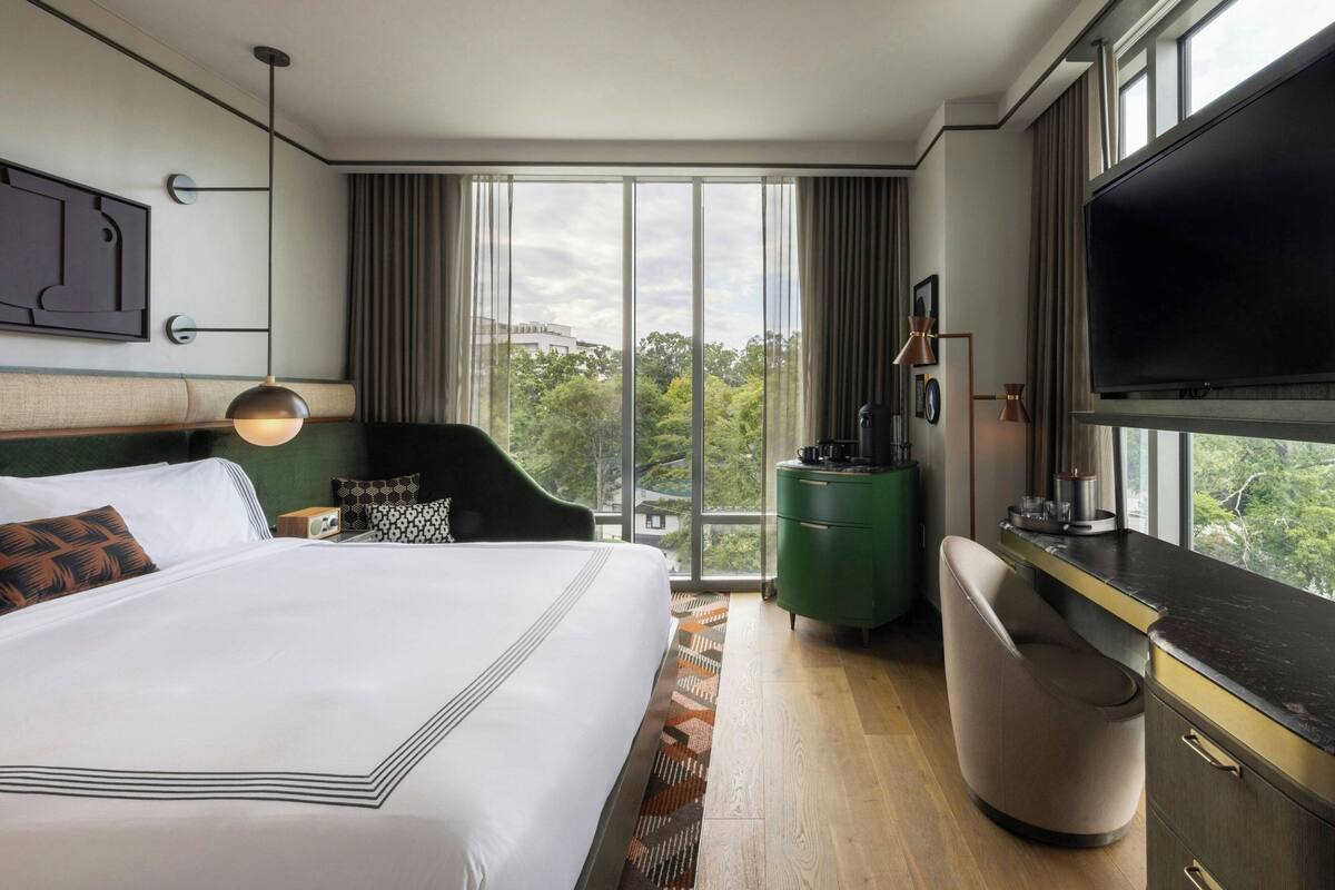 A modern hotel room with a large bed, a desk, a television, and a view of the outdoors.