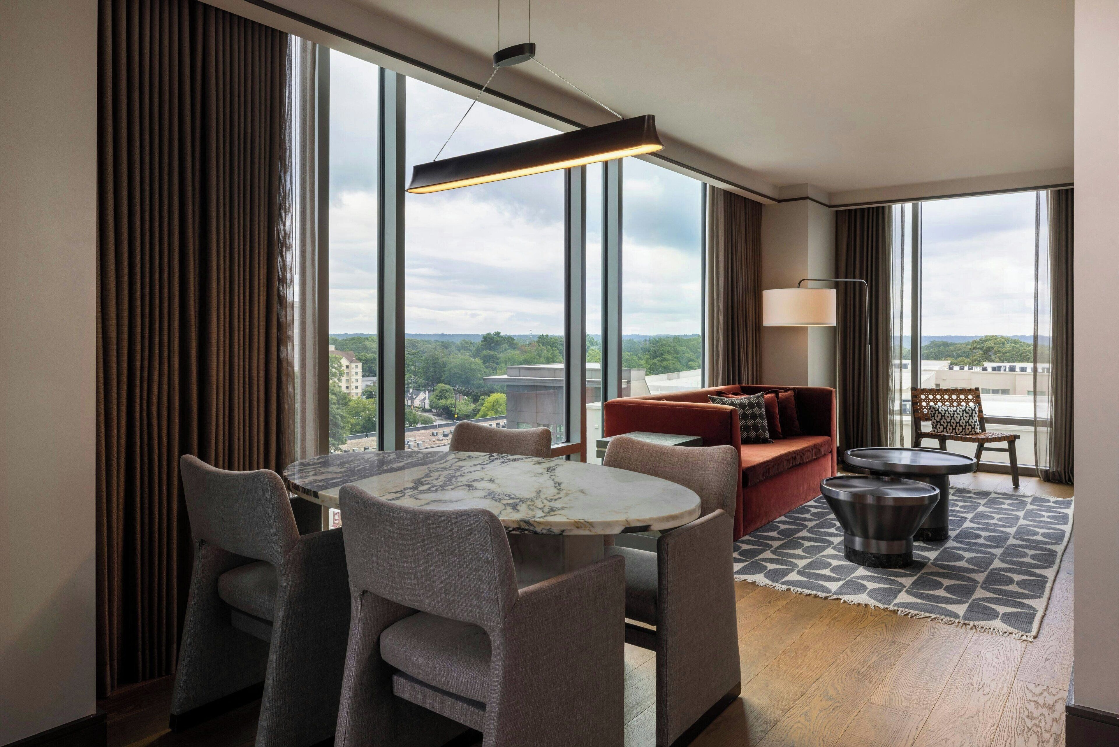 Una habitación de hotel moderna con comedor, sofá y vistas a la ciudad.