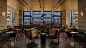 A modern bar area with wooden ceiling, multiple seating options, and shelves displaying bottles. - The Tess, Autograph Collection (Atlanta)