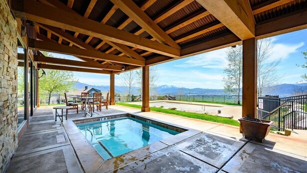 Zona de piscina techada al aire libre con suelo de piedra, vigas de madera y vistas a las montañas.