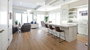 Una cocina moderna con una isla central, taburetes de bar y una zona de comedor con sofá y sillas.
