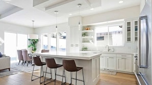 Una cocina moderna con una isla grande, armarios blancos y un refrigerador de acero inoxidable.