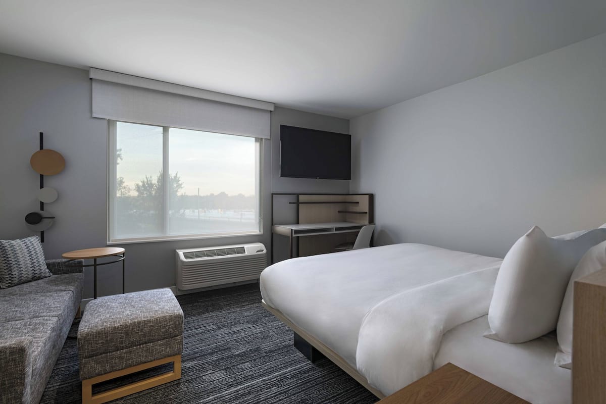 Una habitación de hotel moderna con una cama grande, un sofá, un escritorio y un televisor montado en la pared.
