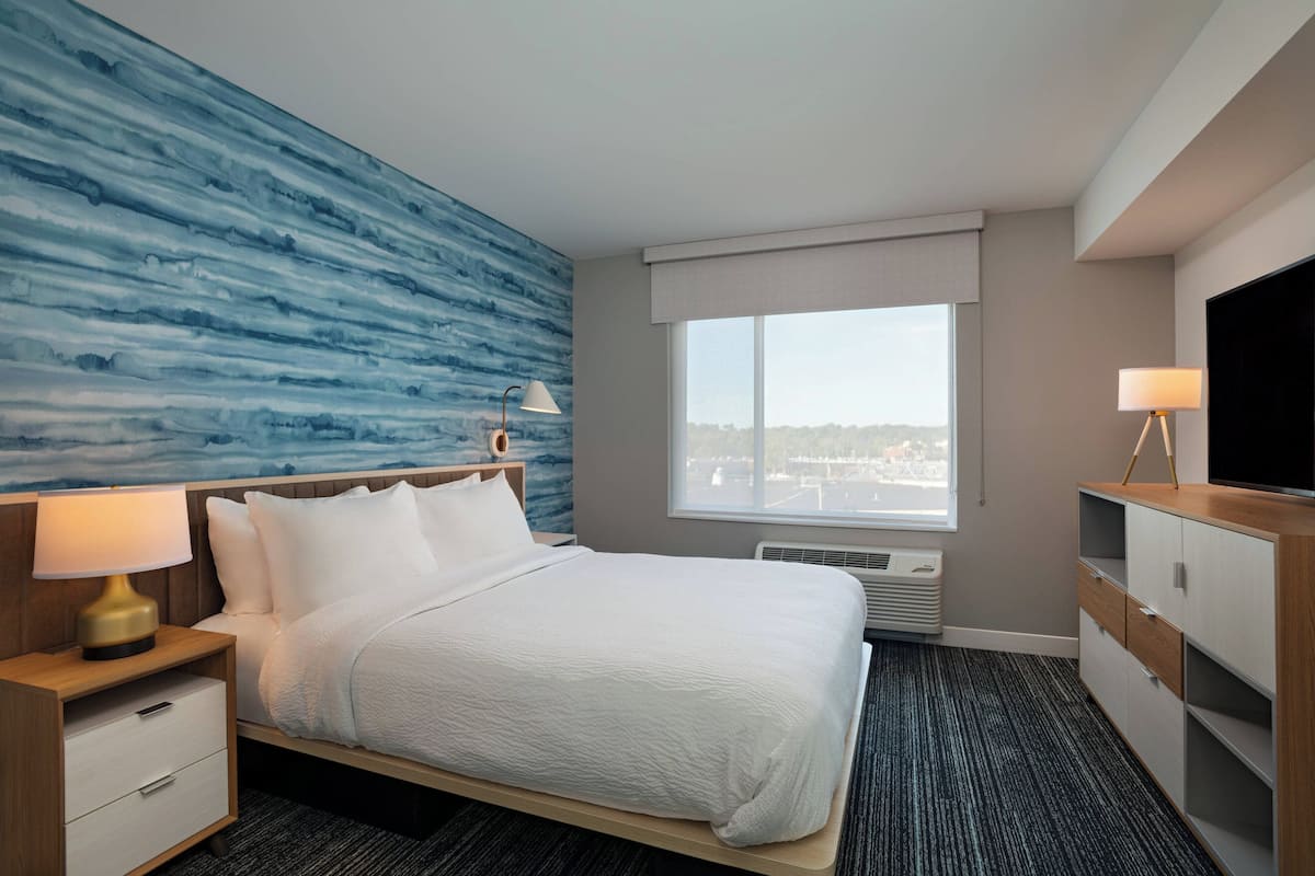 Habitación de hotel con cama, mesita de noche, televisor, ventana con vistas y pared con un diseño azul.