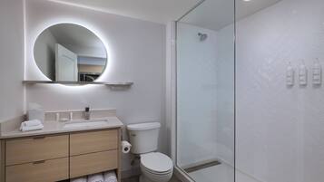 A modern bathroom with a round mirror, a toilet, a sink, and a glass-enclosed shower.