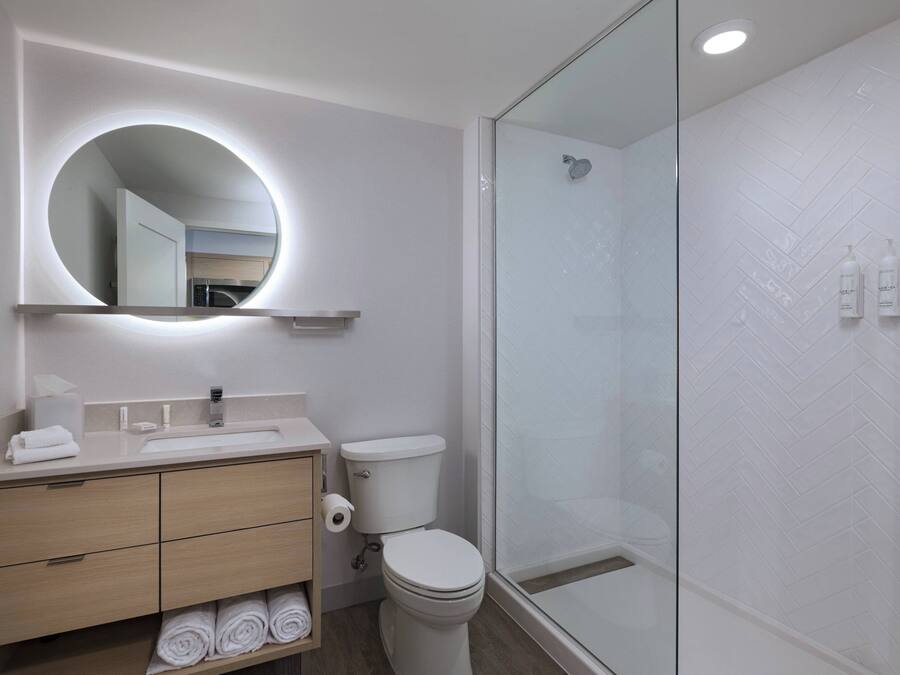 A modern bathroom with a round mirror, a toilet, a sink, and a glass-enclosed shower.