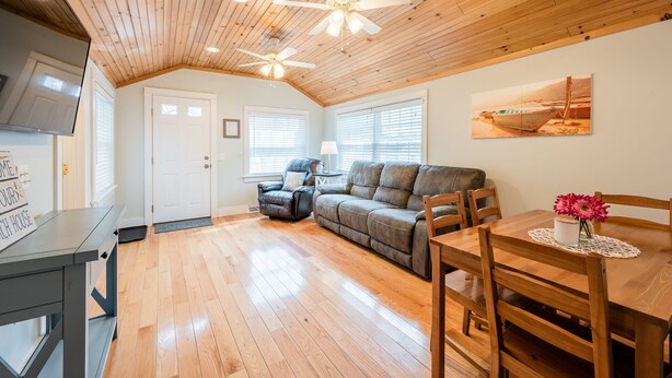 A cozy living room with a wooden ceiling, a gray sofa, a dining table with chairs, and a ceiling fan. - Relaxing Getaway with Town Beach Access (Westerly)