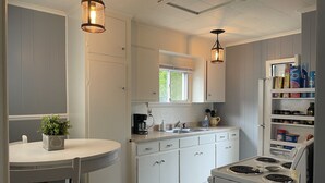 Una cocina compacta con gabinetes blancos, estufa, pileta e iluminación colgante.