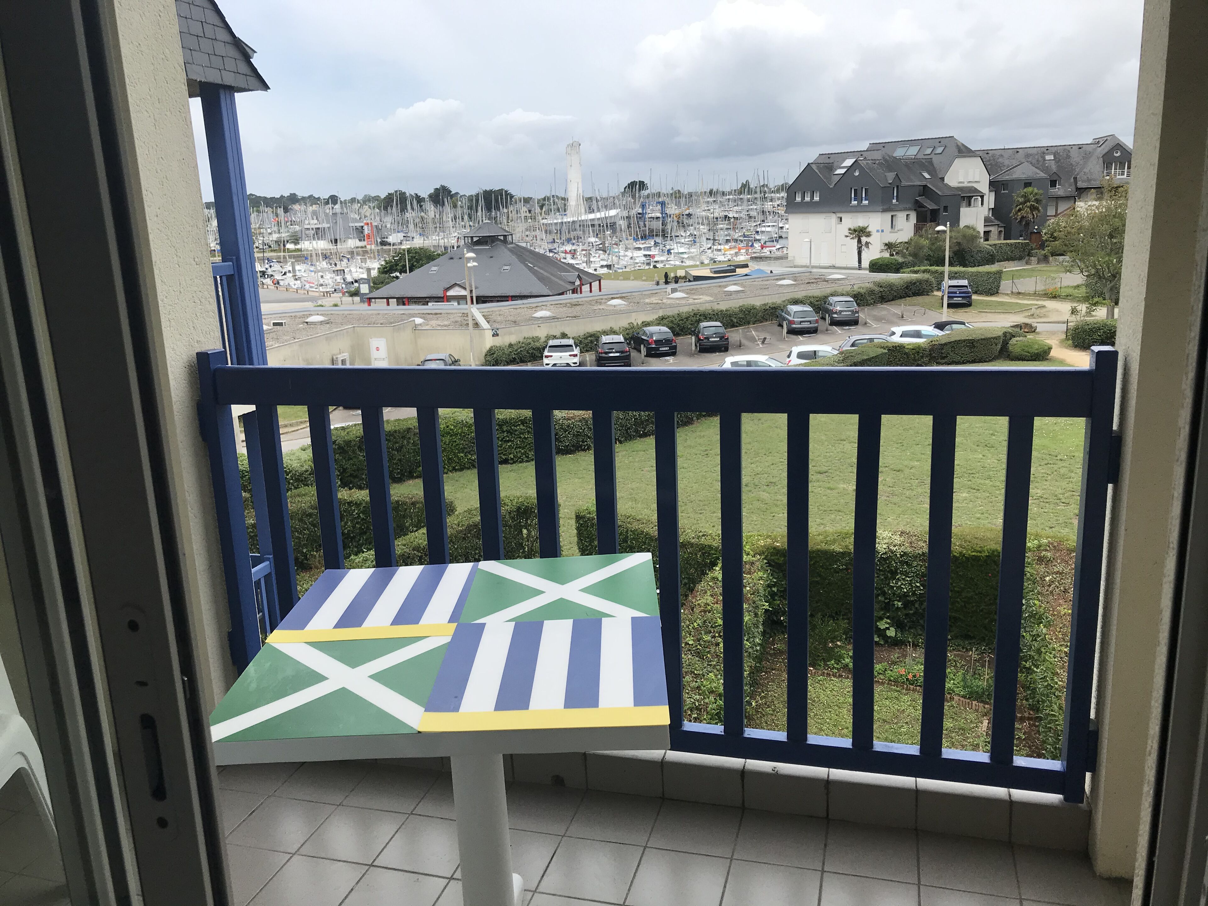 En balkon med udsigt over en lysthavn, parkerede biler og boligbygninger.