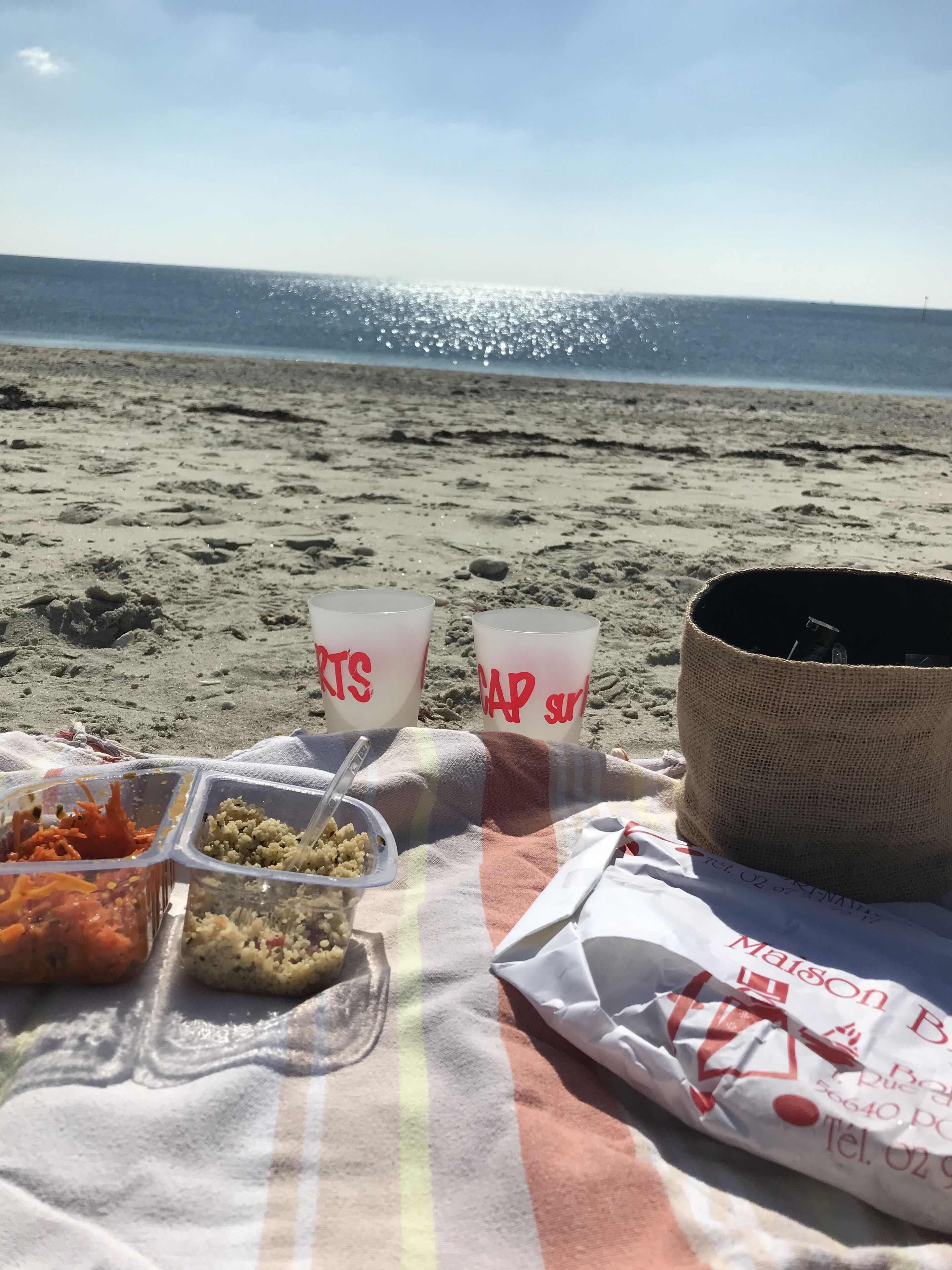 En strand picnic med madkasser, et sugerør og en strandtaske på et tæppe.