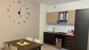 Una cucina moderna con mobili scuri, un fornello e una lavastoviglie. C'è un tavolo da pranzo con sedie e una sveglia a muro.