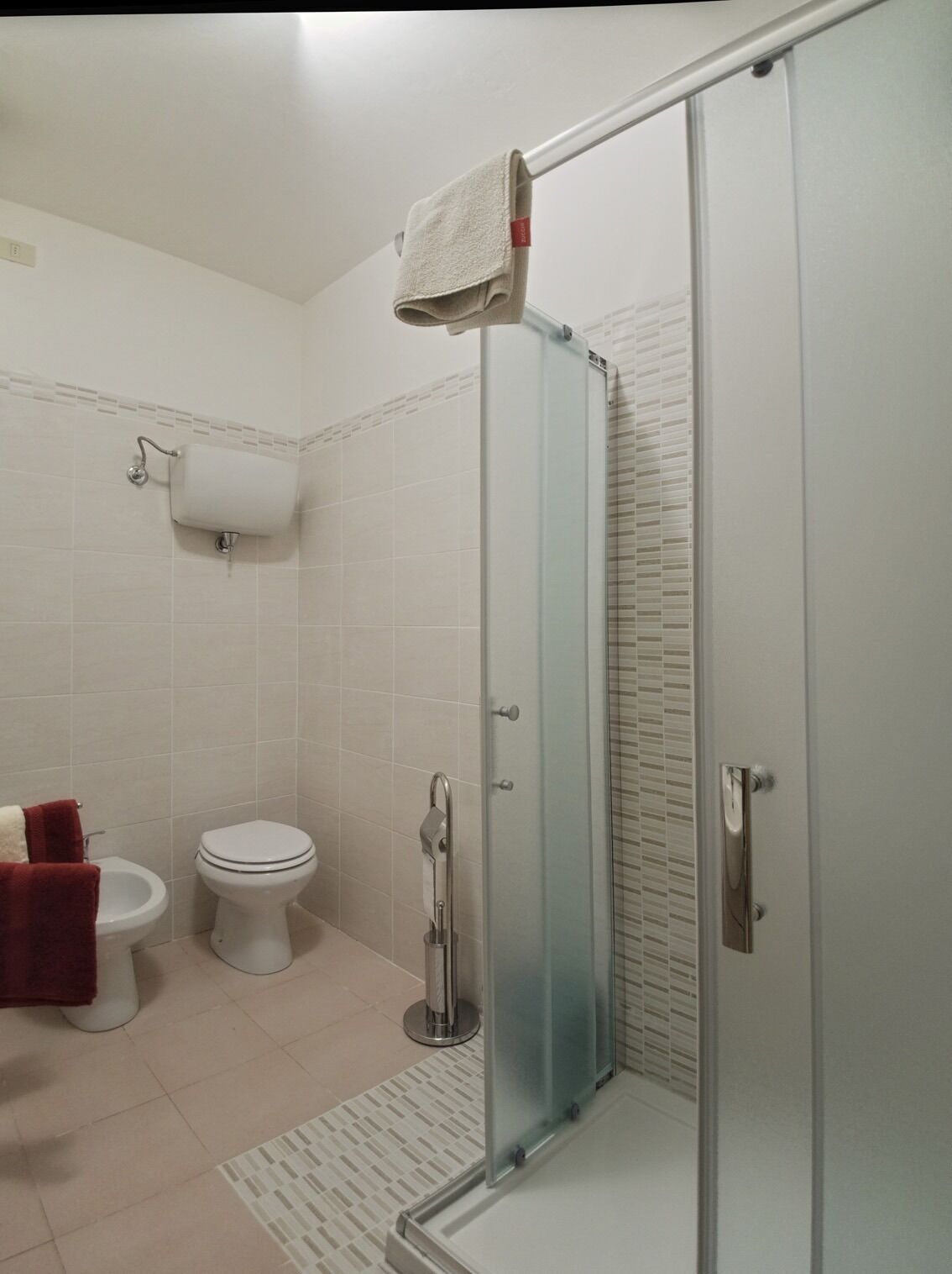 A modern bathroom with a glass-enclosed shower, a toilet, and a bidet.
