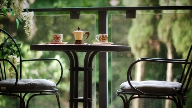 Un balcone con un tavolo apparecchiato per due, con una caffettiera e due tazze, circondato da sedie.