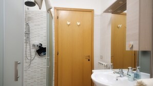 Un bagno con cabina doccia in vetro, una porta in legno, un lavandino con specchio e una lavatrice.