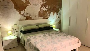 Una camera da letto con una mappa del mondo appesa al muro, un letto con biancheria a motivi e un comodino con una lampada.