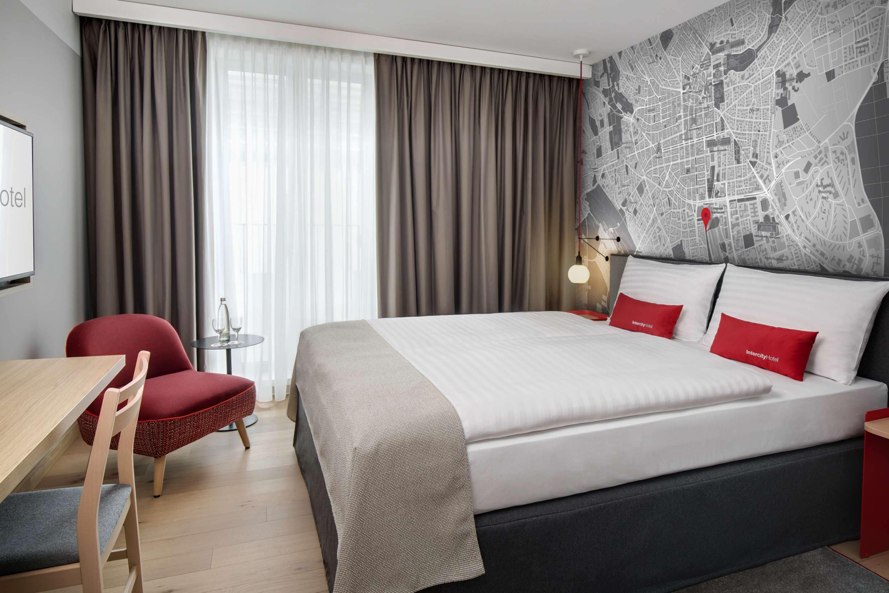 Habitación de hotel con una cama grande, un escritorio, una silla, un mapa en la pared y vistas de la ciudad.