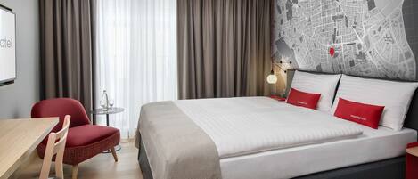 Habitación de hotel con una cama grande, un escritorio, una silla, un mapa en la pared y vistas de la ciudad.