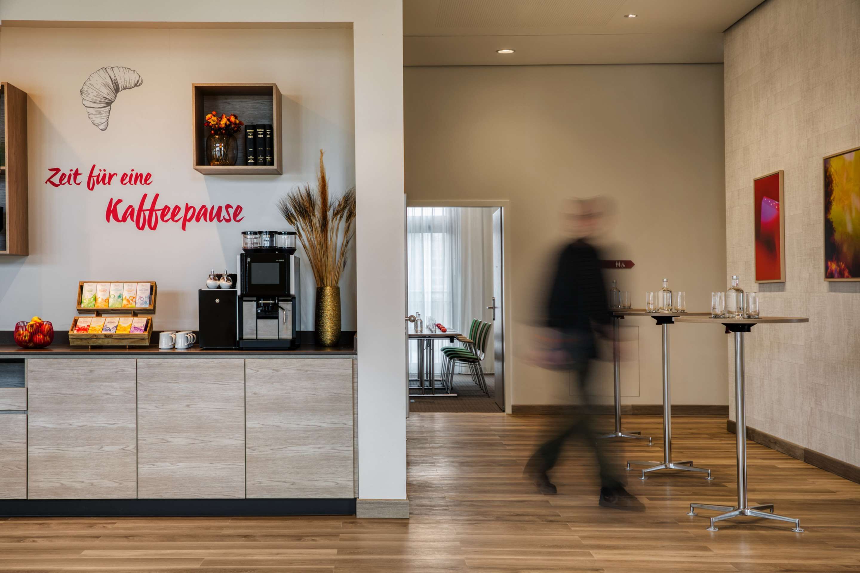 Un vestíbul d'hotel modern amb un racó de cafè, una zona de dinar i un passadís amb taules.