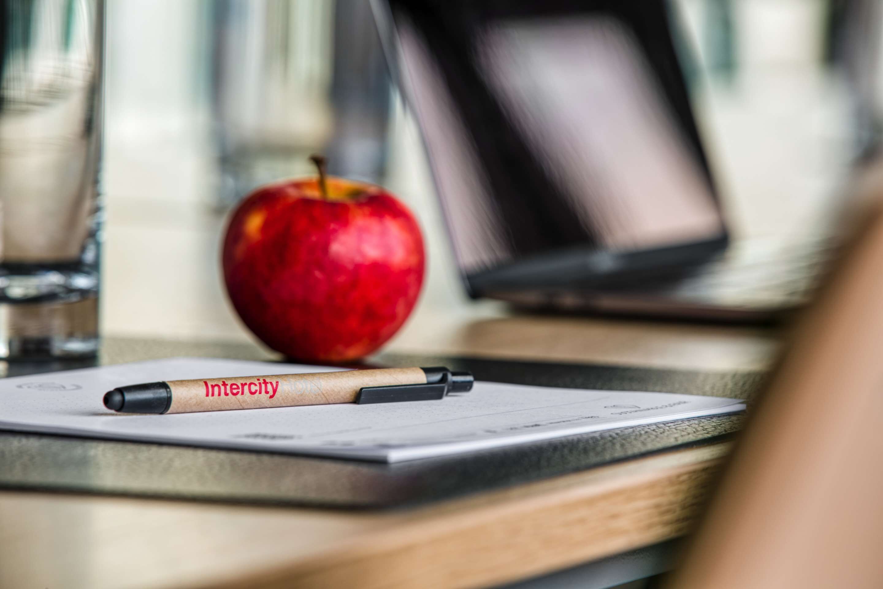 Une pomme rouge, un stylo et une tablette sur une table.