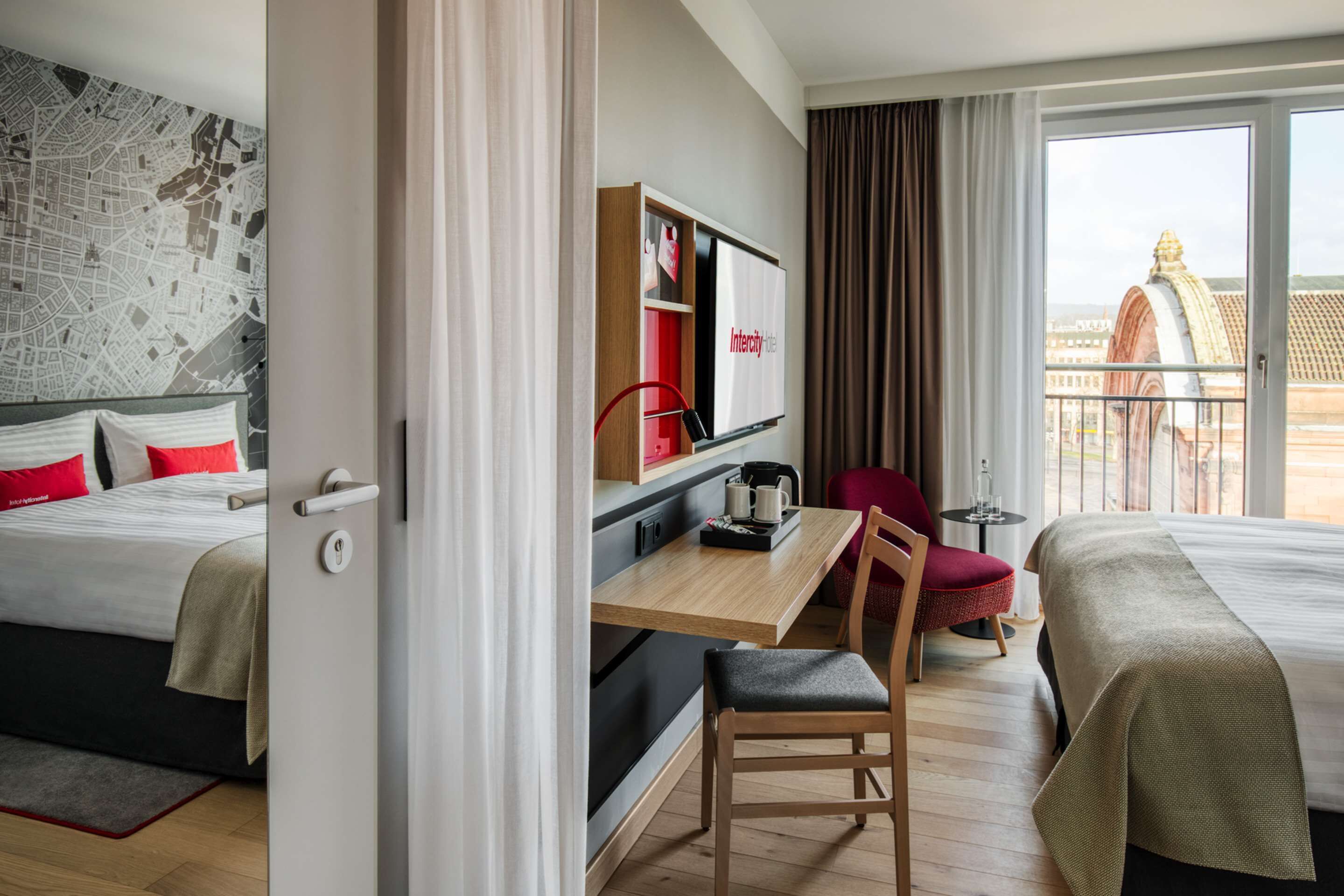Hotellihuone, jossa on kaksi sänkyä, työpöytä tuolilla, pieni pöytä, televisio ja suuret ikkunat, joista avautuu näkymä kaupungin ylle.