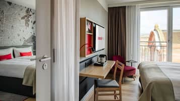Hotellihuone, jossa on kaksi sänkyä, työpöytä tuolilla, pieni pöytä, televisio ja suuret ikkunat, joista avautuu näkymä kaupungin ylle.