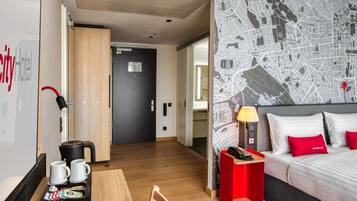 Habitación de hotel con una cama, una mesita de noche roja, una lámpara y una bandeja con tazas y un hervidor.