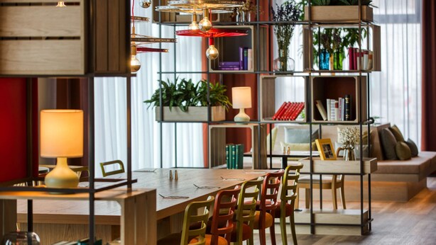 A modern interior with a wooden dining table, multiple chairs, a bookshelf, and a sofa. - IntercityHotel Wiesbaden (Wiesbaden)
