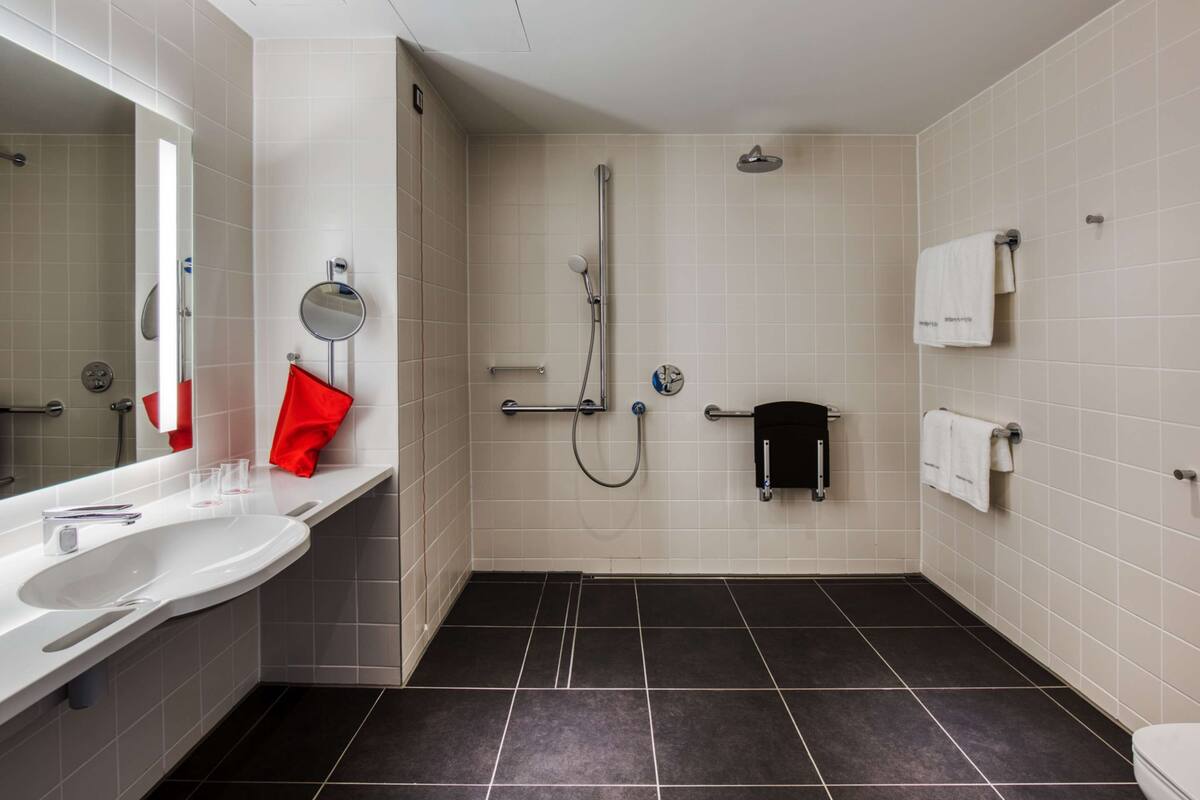 Een moderne badkamer met een wit wastafelmeubel, een spiegel, een rode handdoek, een douchegedeelte en een toilet.
