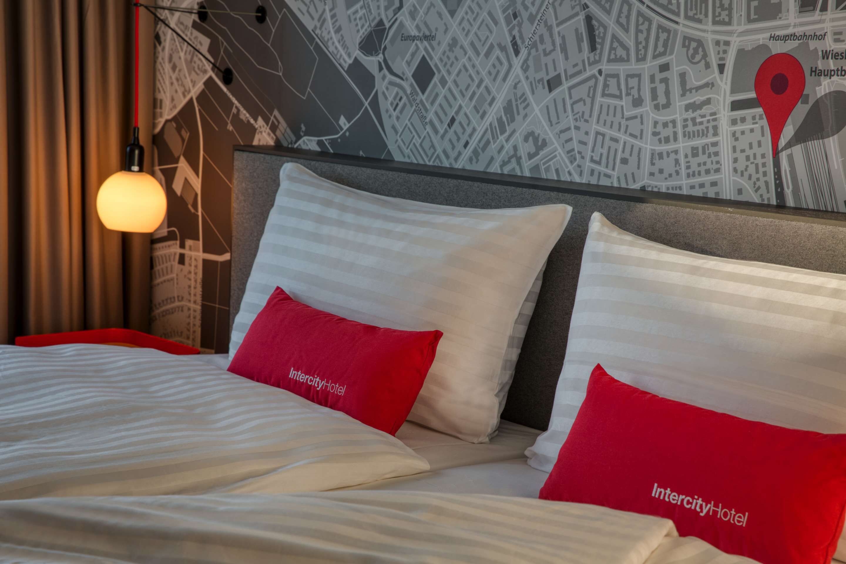 Een hotelkamer met een bed, rode en witte kussens, een kaart aan de muur en een hanglamp.