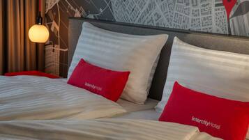 Een hotelkamer met een bed, rode en witte kussens, een kaart aan de muur en een hanglamp.