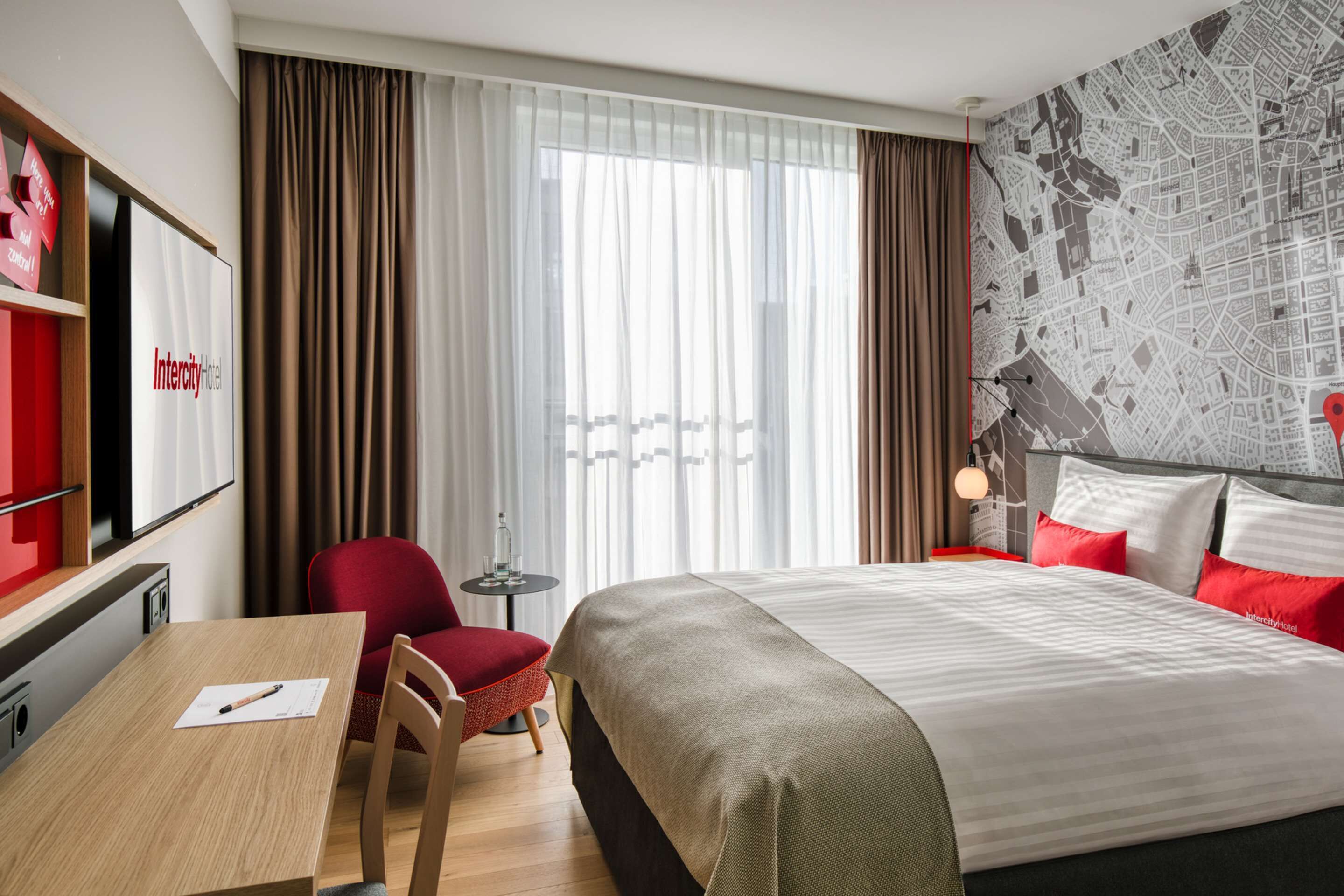 Ein Hotelzimmer mit Bett, Schreibtisch, Stuhl, kleinem Tisch und einer Karte an der Wand.