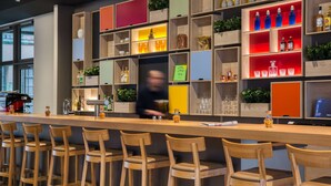 A bar area with wooden chairs, shelves with bottles and glasses, and a bar counter. - IntercityHotel Wiesbaden (Wiesbaden)