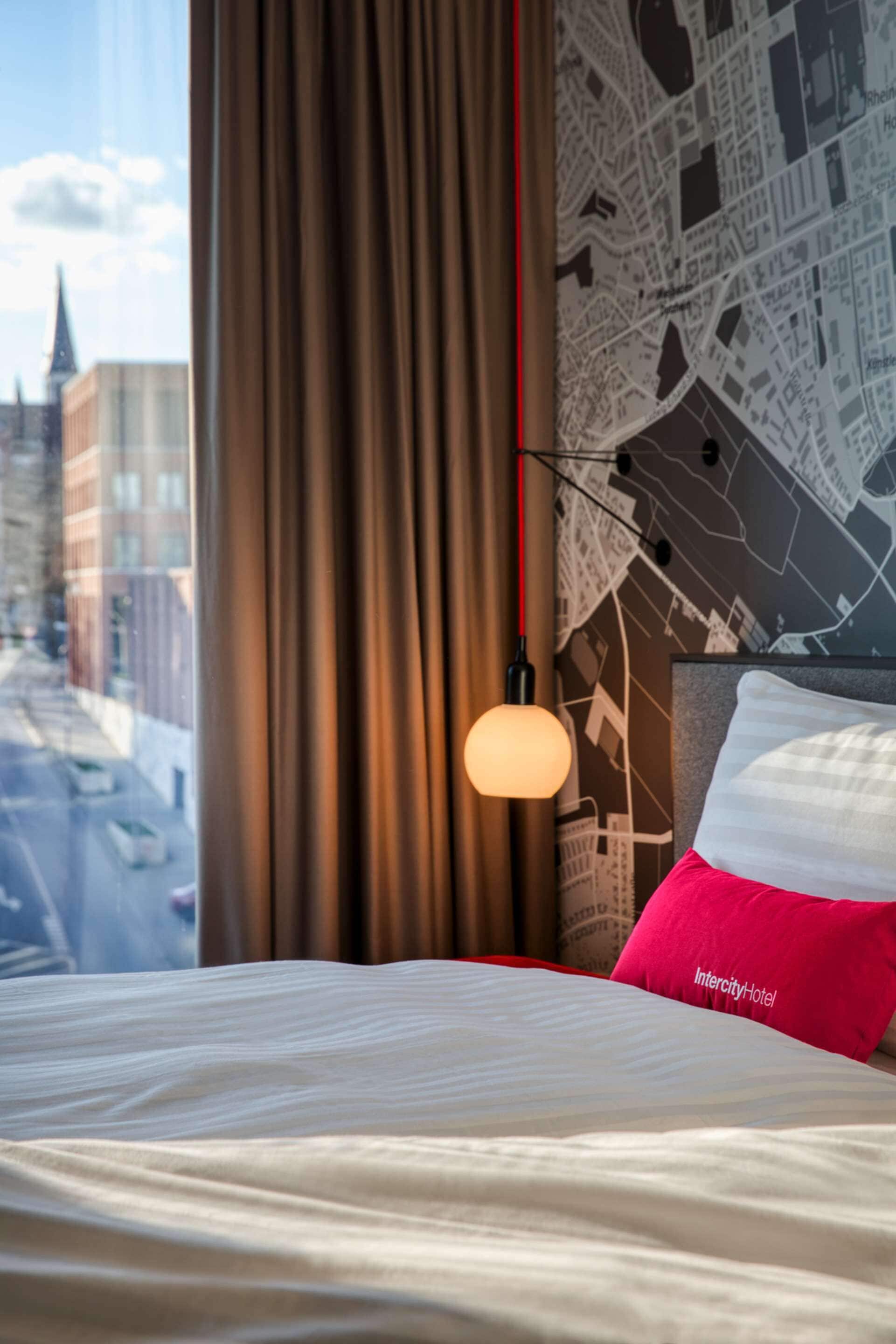 Ein Hotelzimmer mit einem Bett, einer Karte an der Wand und Blick auf Gebäude vor dem Fenster.