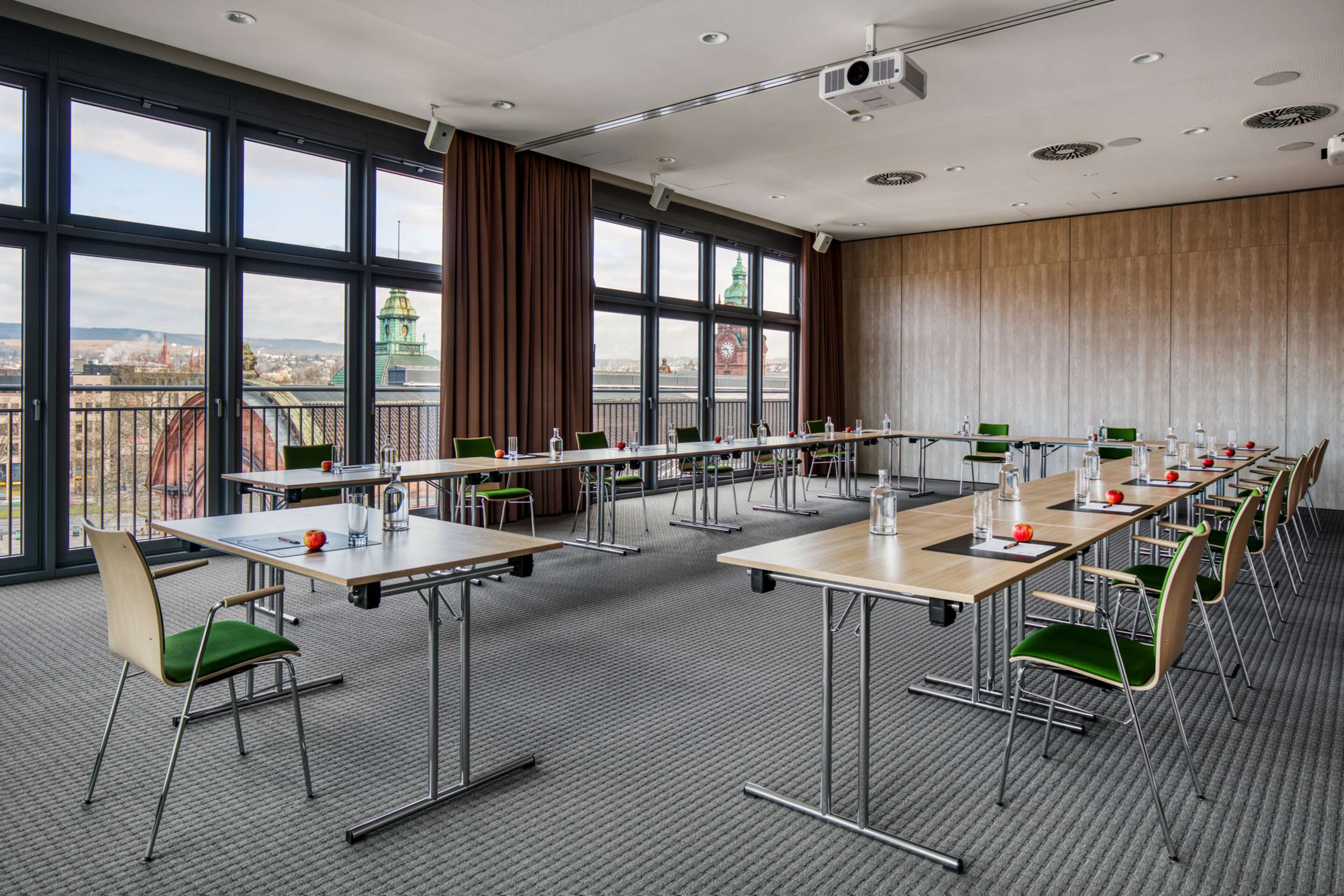 Un salón de conferencias con amplias ventanas, techo alto y vista a la ciudad.