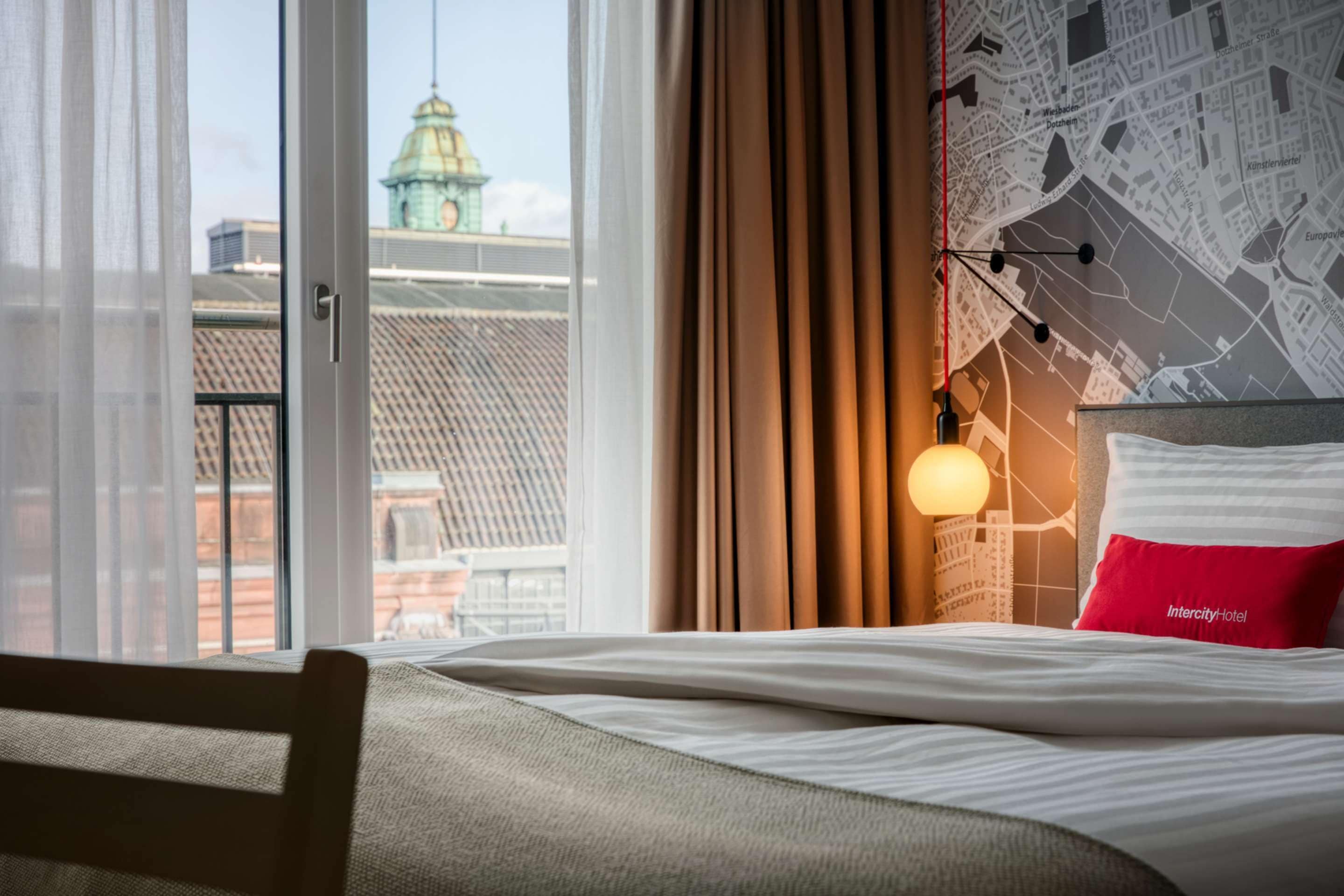 Hotelkamer met een bed, uitzicht op een stadsbeeld door een groot raam, en een kaart aan de muur.