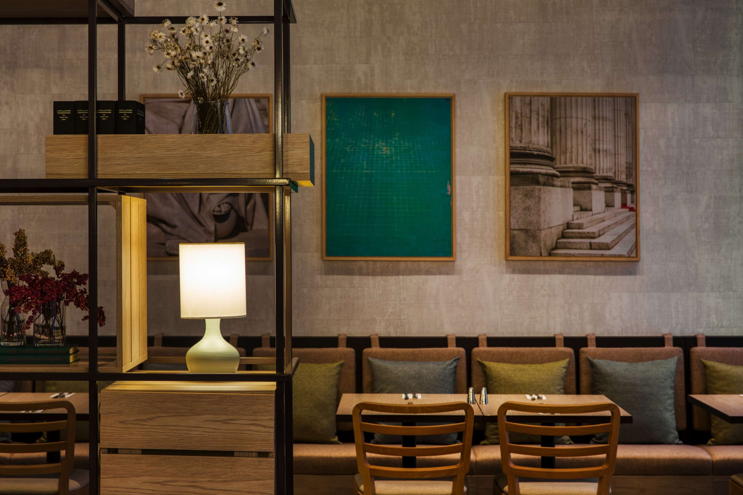 Un interior moderno con una zona de estar con banca de madera, una mesa con lámpara y obras de arte enmarcadas en la pared.