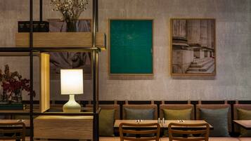 Un interior moderno con una zona de estar con banca de madera, una mesa con lámpara y obras de arte enmarcadas en la pared.