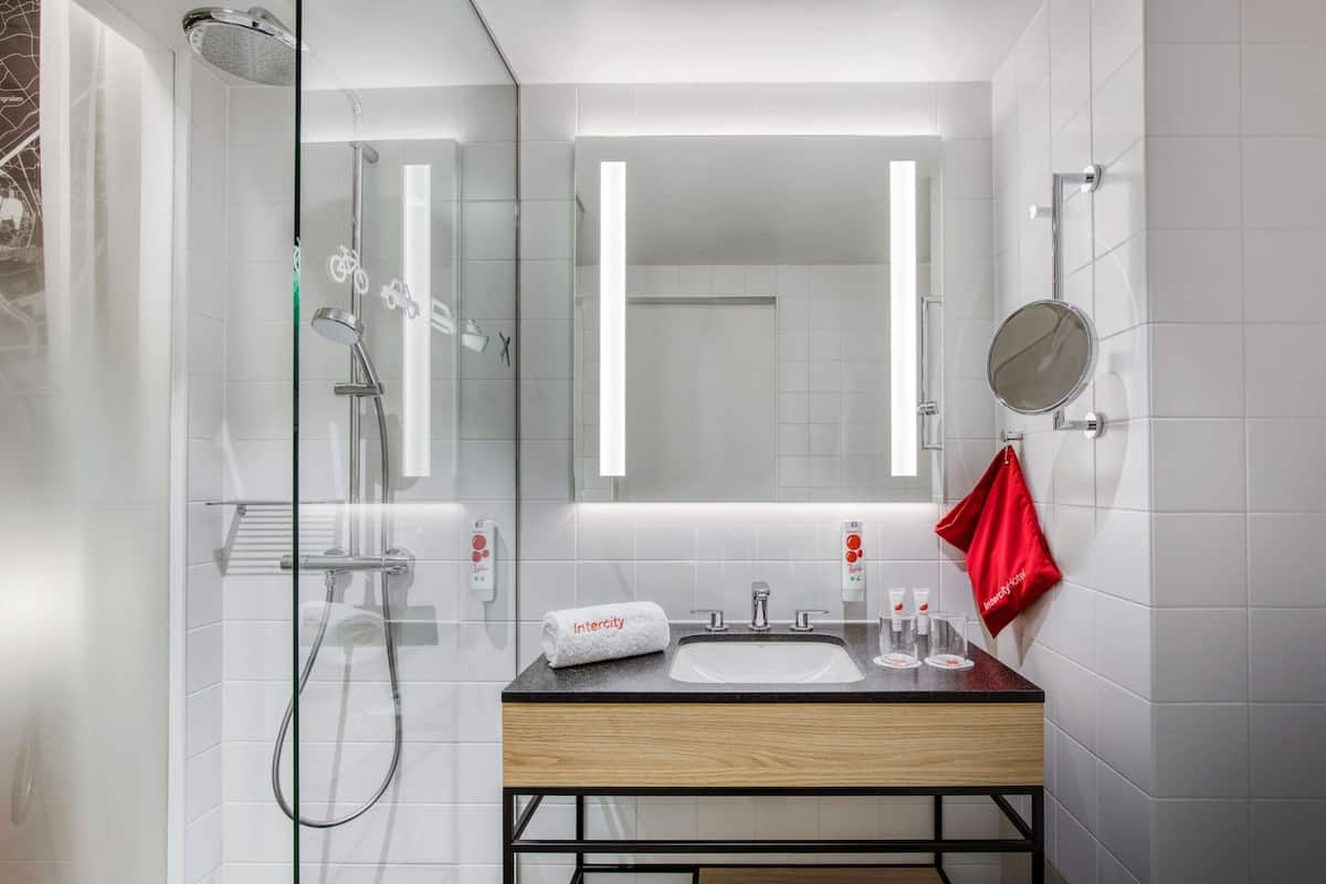 Een moderne badkamer met een douchecabine van glas, een houten wastafelmeubel met een wastafel en een grote spiegel.