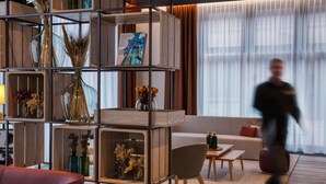 A modern living room with a sectional sofa, a coffee table, and a bookshelf with decorative items. - IntercityHotel Wiesbaden (Wiesbaden)