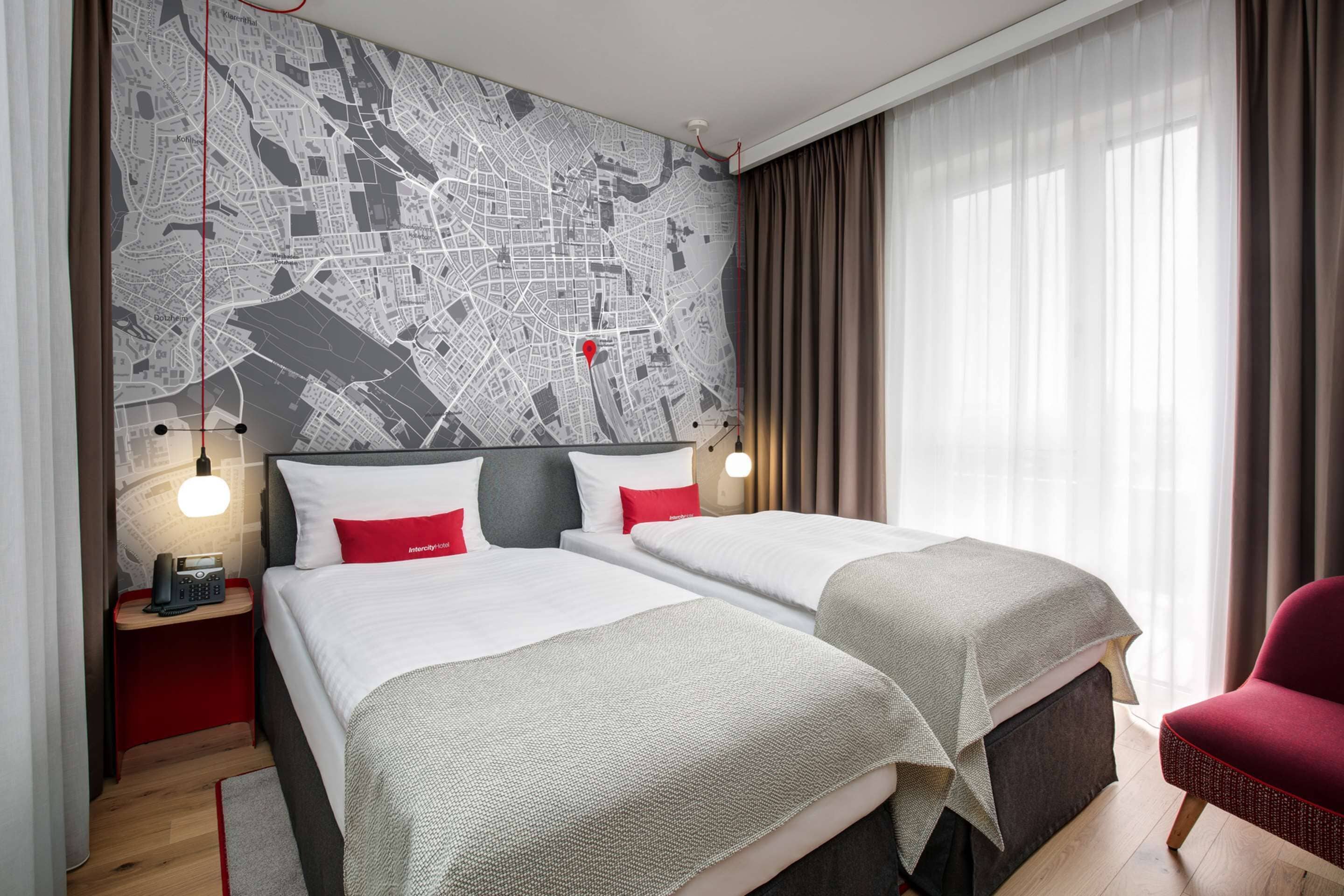 A hotel room with two beds, a map on the wall, a red chair, and a nightstand with a phone.