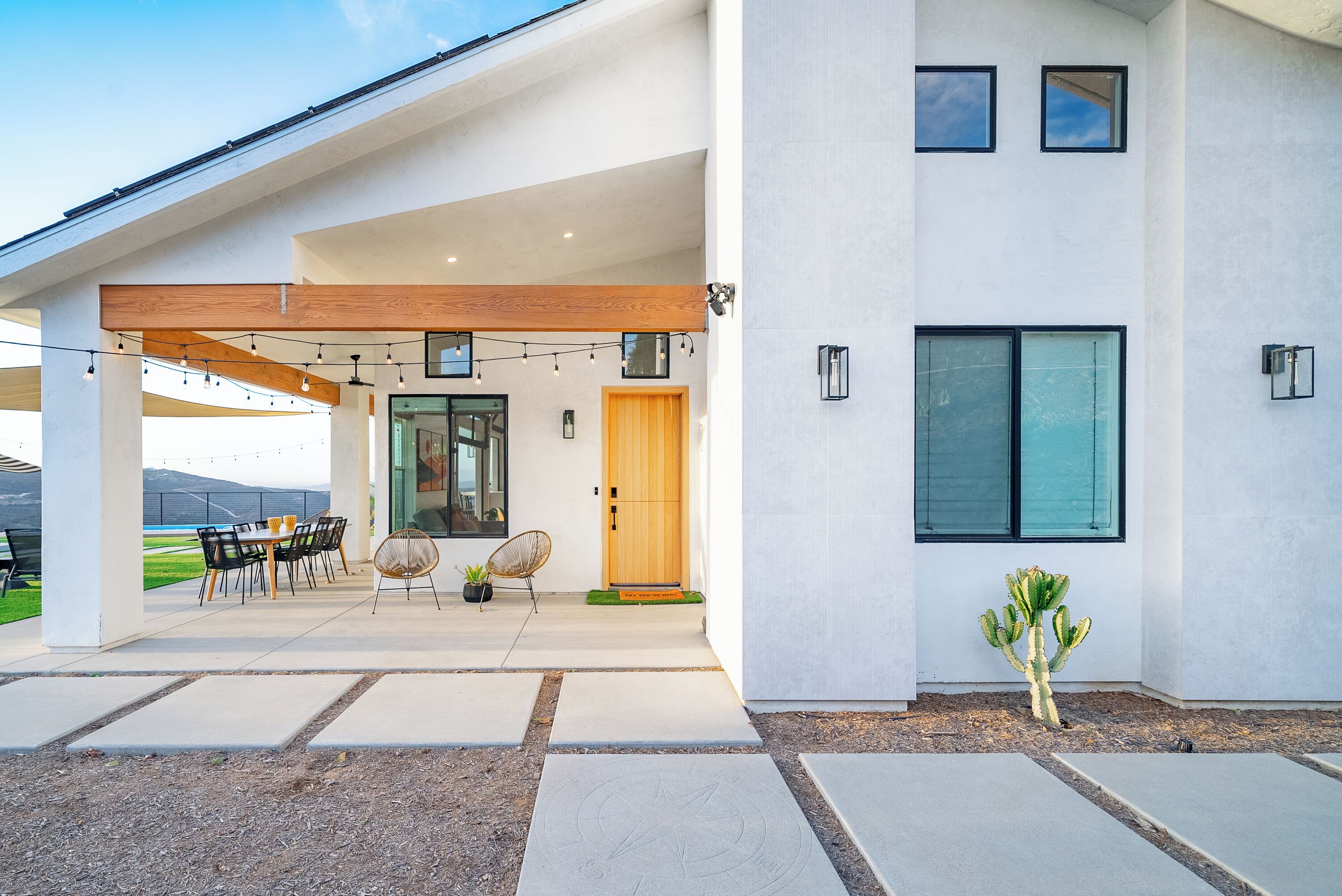 A modern house with a patio, outdoor seating, and a cactus in the garden.