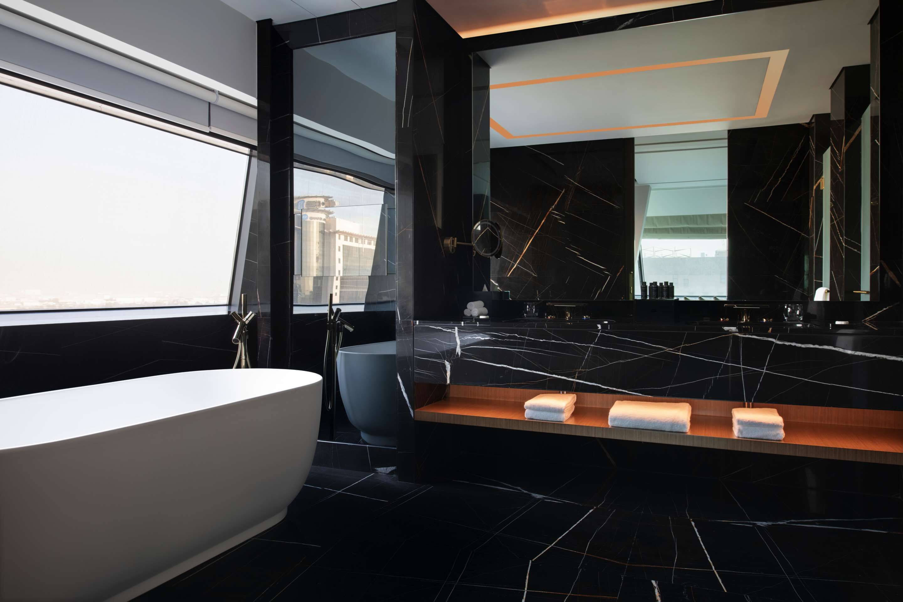 A modern bathroom with a freestanding bathtub, a large mirror, and a vanity with towels.