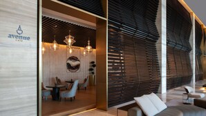 A modern interior with a wooden wall, a seating area with round tables and chairs, and a curved wall with horizontal slats. - Steigenberger Hotel Doha (Doha)
