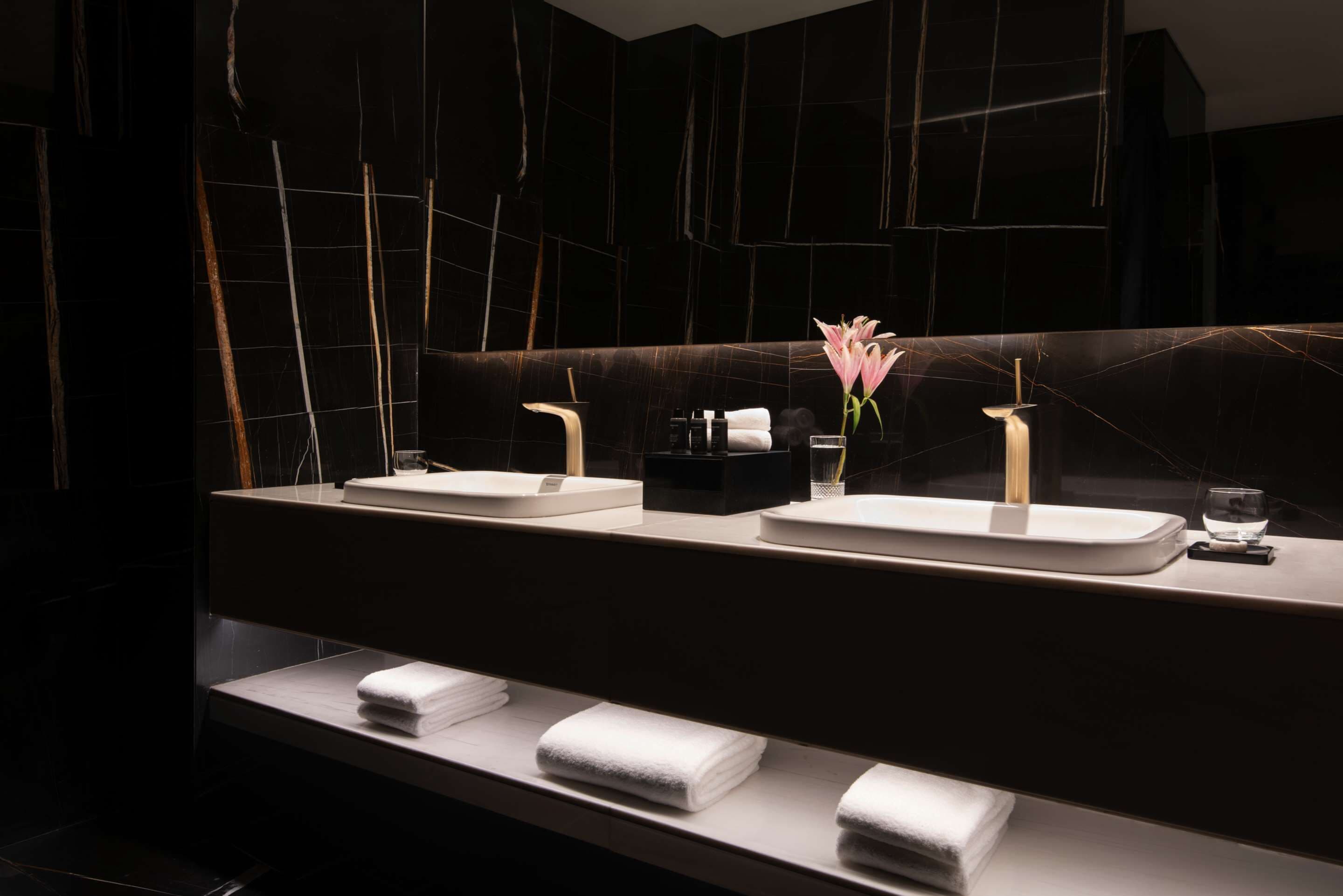 A modern bathroom with two sinks, a large mirror, and neatly folded towels on a shelf.