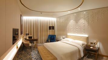A hotel room with a bed, a desk, a chair, a mirror, and a wall with a decorative panel.