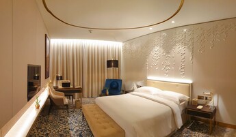 A hotel room with a bed, a desk, a chair, a mirror, and a wall with a decorative panel.